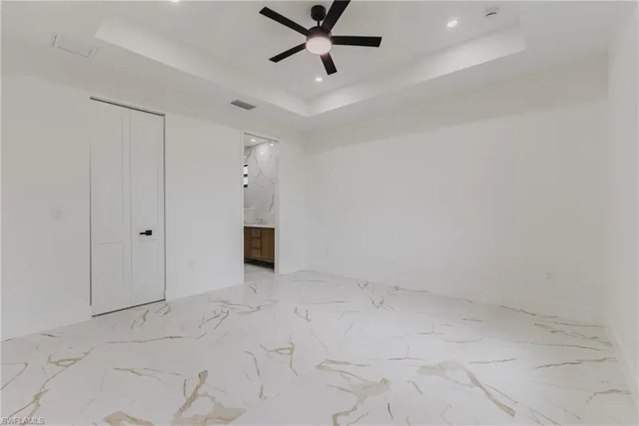 Unfurnished bedroom with a raised ceiling, a closet, a ceiling fan, recessed lighting, and ensuite bath