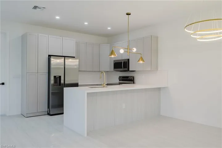 Kitchen featuring appliances with stainless steel finishes, a peninsula, decorative backsplash, light stone counters, and gray cabinetry