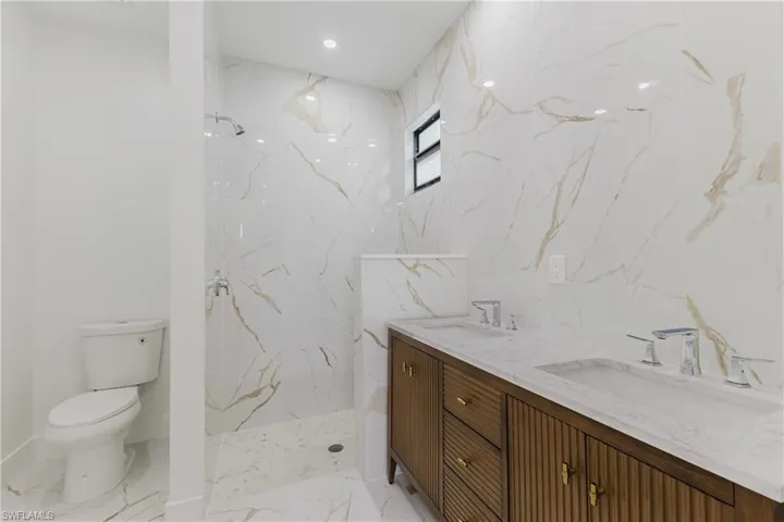 Full bathroom featuring a marble finish shower, double vanity, stone wall, light marble finish flooring, and recessed lighting