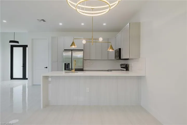 Kitchen with appliances with stainless steel finishes, decorative backsplash, hanging light fixtures, a peninsula, and light stone counters