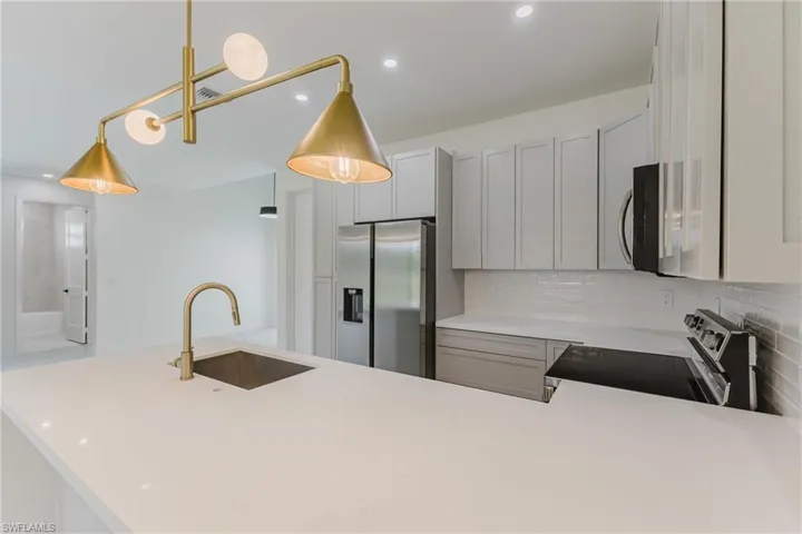 Kitchen featuring gray cabinets, stainless steel appliances, recessed lighting, decorative light fixtures, and a peninsula