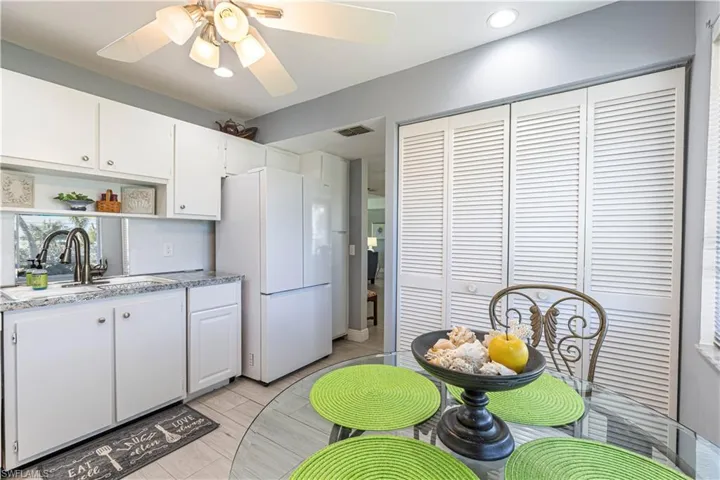 Kitchen featuring white cabinetry, freestanding refrigerator, light stone countertops, ceiling fan, and open shelves