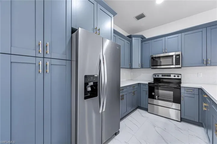 Kitchen featuring blue cabinets, stainless steel appliances, tasteful backsplash, and light tile floors