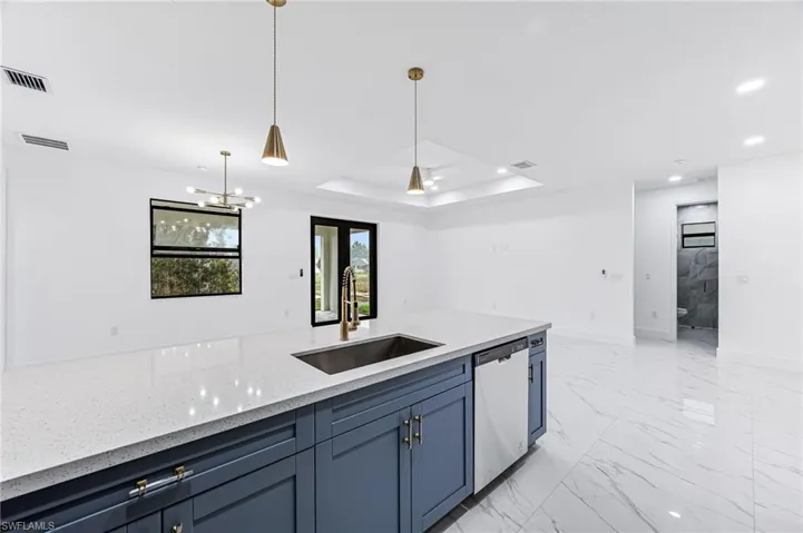 Kitchen featuring light tile flooring, dishwasher, a tray ceiling, light stone countertops, and sink