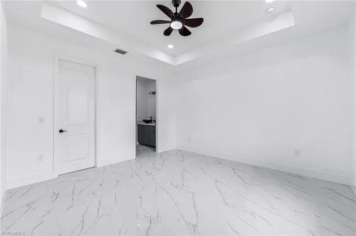 Unfurnished bedroom with a tray ceiling, ensuite bathroom, ceiling fan, and light tile floors