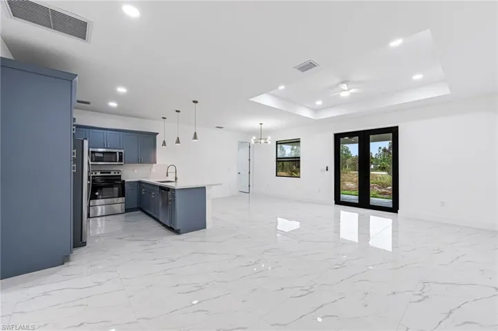 Kitchen featuring hanging light fixtures, appliances with stainless steel finishes, a tray ceiling, and light tile flooring