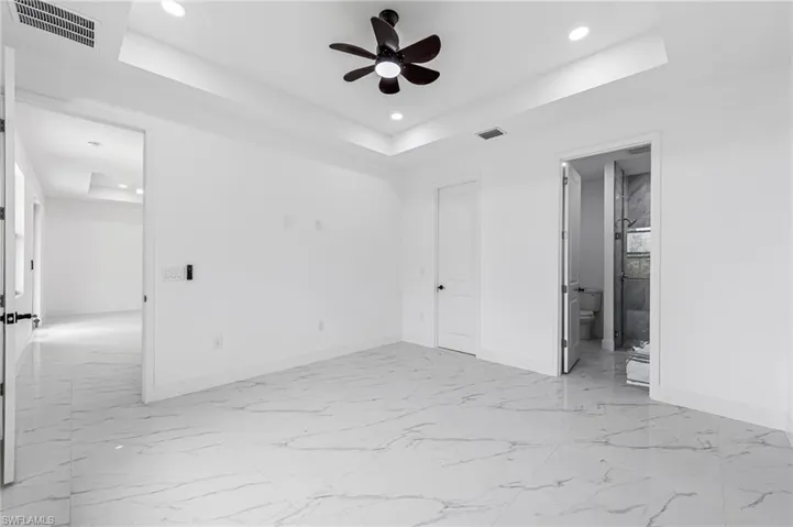 Empty room featuring tile flooring, ceiling fan, and a tray ceiling