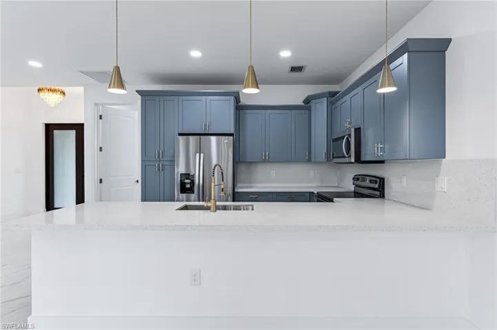 Kitchen with appliances with stainless steel finishes, hanging light fixtures, and backsplash