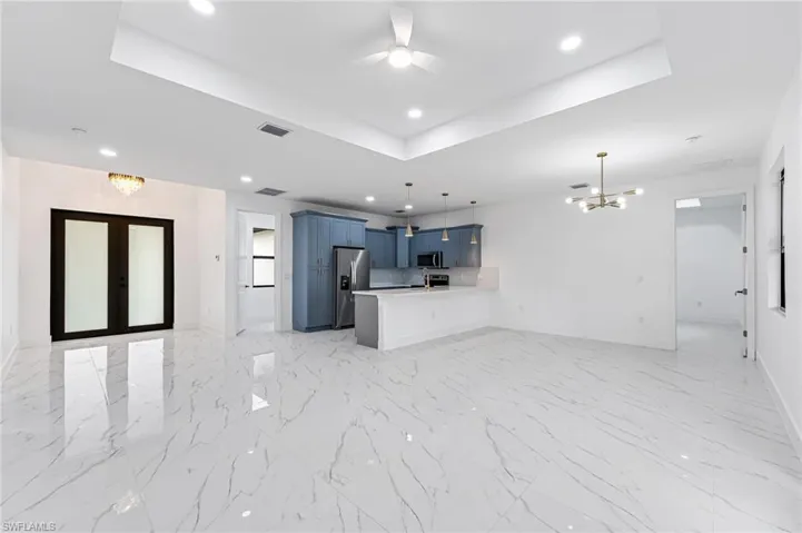 Unfurnished living room with ceiling fan with notable chandelier, light tile floors, and a raised ceiling