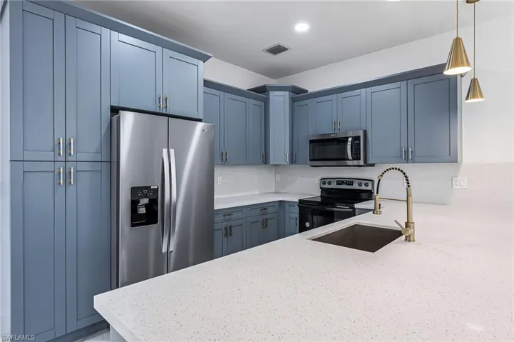 Kitchen with appliances with stainless steel finishes, light stone counters, pendant lighting, sink, and tasteful backsplash