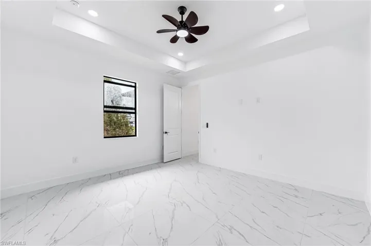 Unfurnished room with a tray ceiling, light tile flooring, and ceiling fan