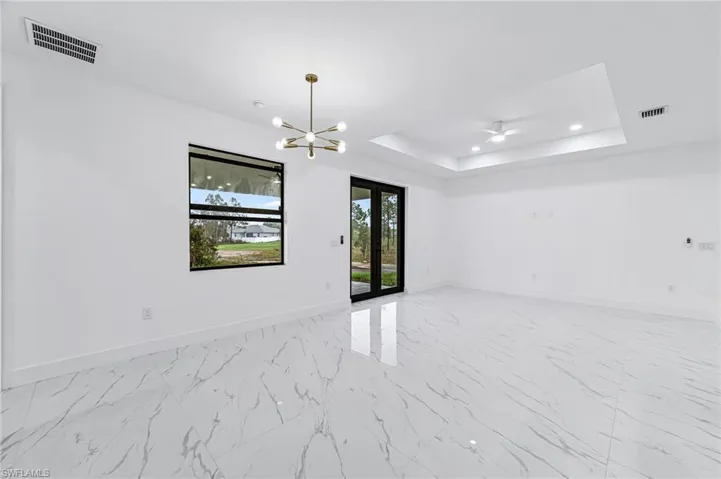 Spare room with french doors, a chandelier, light tile flooring, and a raised ceiling