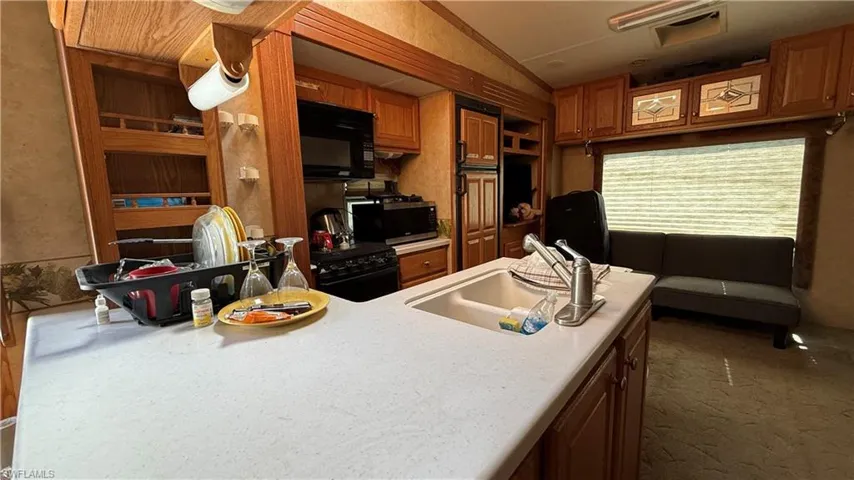 Kitchen featuring brown cabinetry, black microwave, and light countertops
