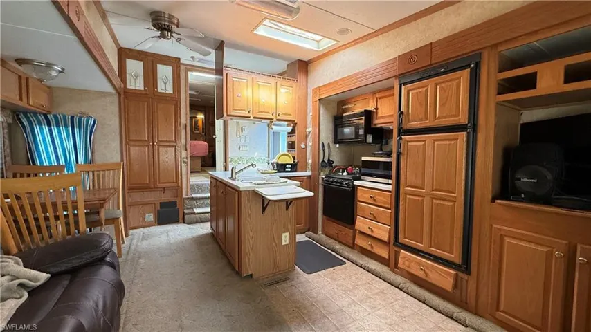 Kitchen featuring a ceiling fan, light countertops, brown cabinetry, stainless steel microwave, and paneled refrigerator
