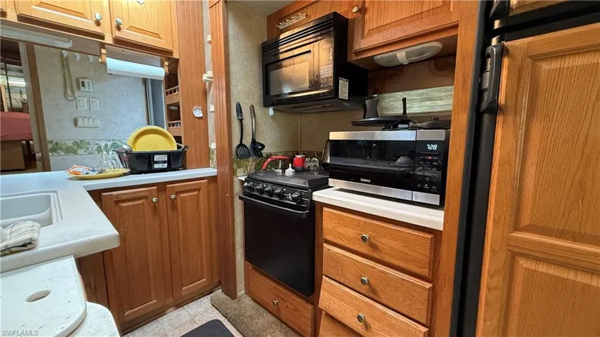 Kitchen with light countertops, brown cabinetry, and black appliances