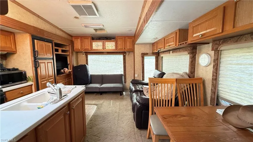 Kitchen featuring brown cabinetry, light countertops, stainless steel microwave, and light carpet