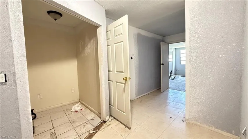 Hallway featuring light tile patterned flooring, a textured wall, and a textured ceiling