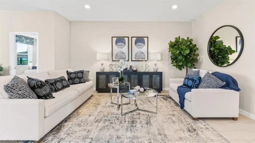 Spacious living area featuring light-toned walls, recessed lighting, and light-tone flooring partially covered by an area rug