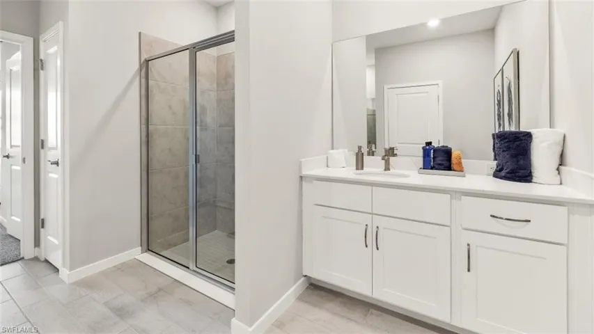 Bathroom with a white double vanity featuring a single undermount sink, a large mirror, and quartz countertops