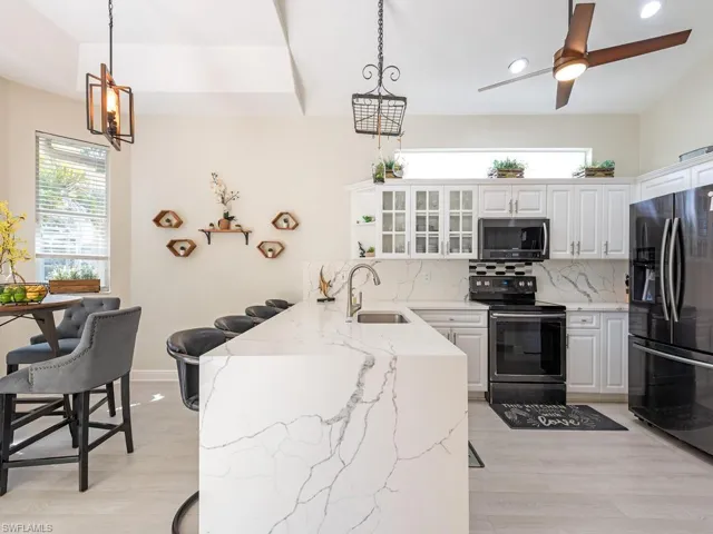 Kitchen featuring a waterfall-edge island with seating, white shaker cabinetry, stainless steel appliances, and wood-finish flooring