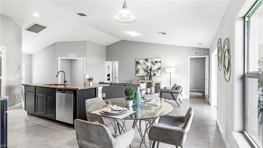Dining area featuring plenty of natural light, sink, light tile flooring, and vaulted ceiling