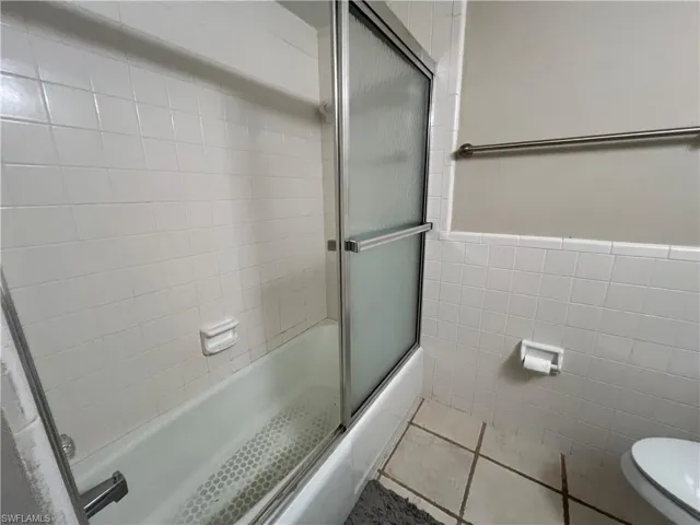 Bathroom with enclosed tub / shower combo, tile walls, tile patterned flooring, and toilet