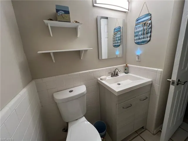 Bathroom with tile walls, tile patterned flooring, vanity, and toilet