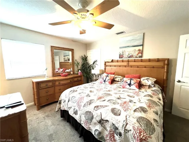 Bedroom featuring ceiling fan, light colored carpet, and a textured ceiling