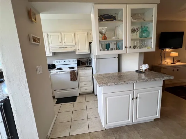 Kitchen featuring white cabinets, white appliances, and light tile patterned flooring
