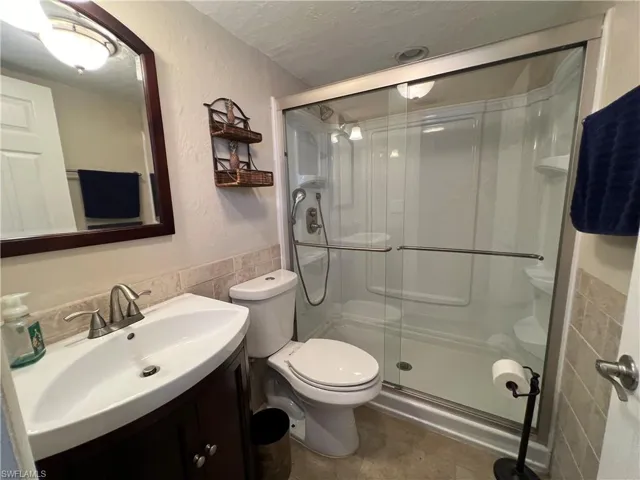 Bathroom with tile walls, a shower with shower door, vanity, a textured ceiling, and toilet