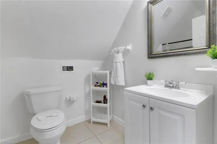 Ensuite Bathroom with tile patterned flooring, vanity, lofted ceiling, and toilet