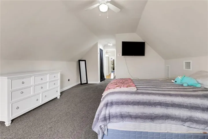 Bedroom with vaulted ceiling, dark carpet, and ceiling fan