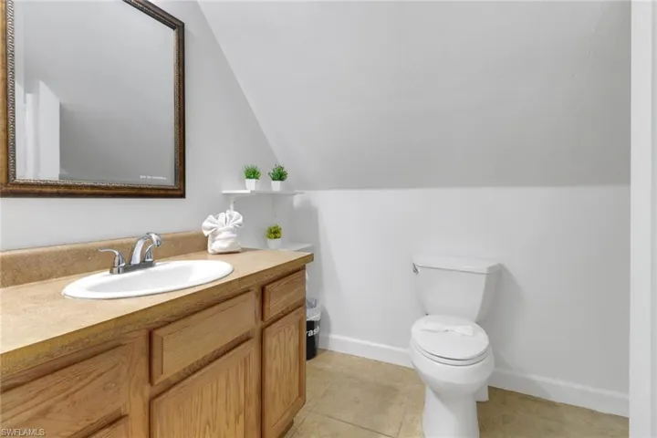 Bathroom featuring tile patterned flooring, vanity, vaulted ceiling, and toilet
