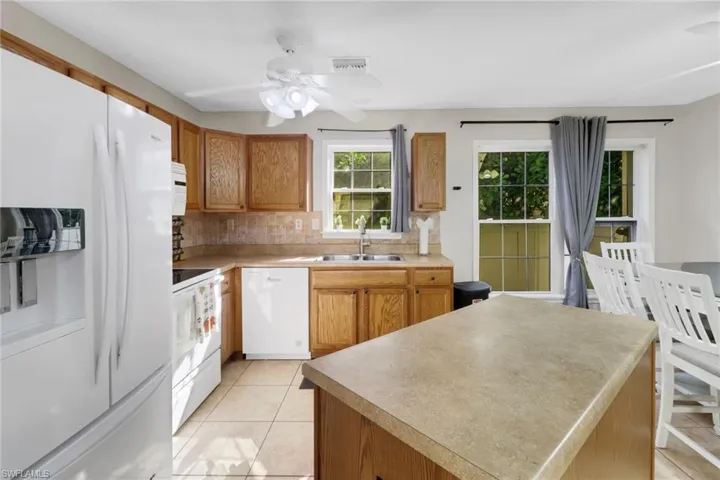 Kitchen featuring white appliances, sink, decorative backsplash, light tile patterned floors, and a kitchen island