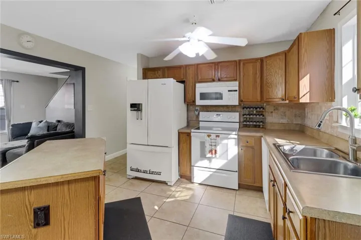 Kitchen with backsplash, white appliances, ceiling fan, sink, and light tile patterned floors