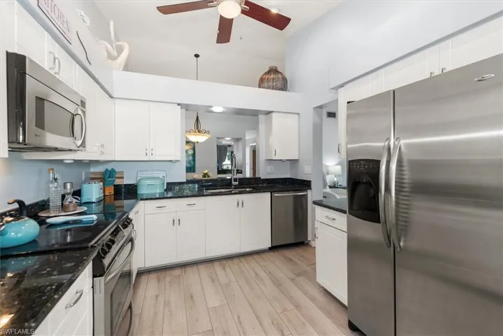 Kitchen featuring stainless steel appliances, dark stone counters, white cabinets, ceiling fan, and a high ceiling