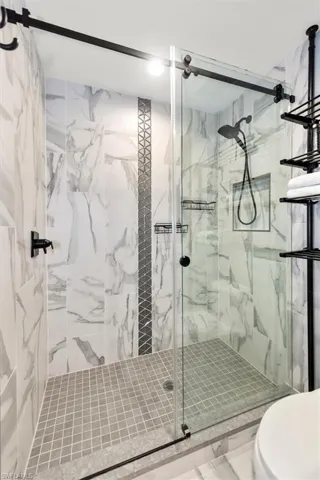 Full bathroom with a marble finish shower and toilet