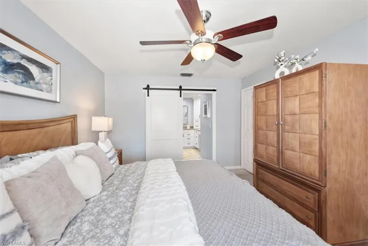 Bedroom featuring a barn door, ensuite bath, and a ceiling fan