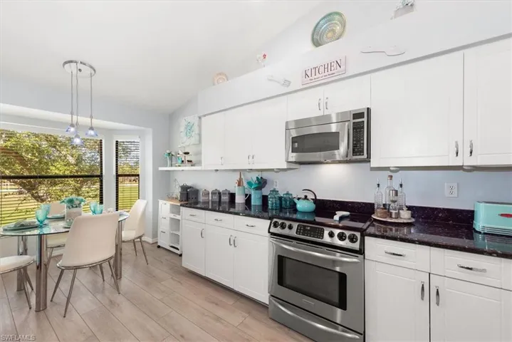 Kitchen featuring appliances with stainless steel finishes, vaulted ceiling, white cabinets, dark stone counters, and pendant lighting