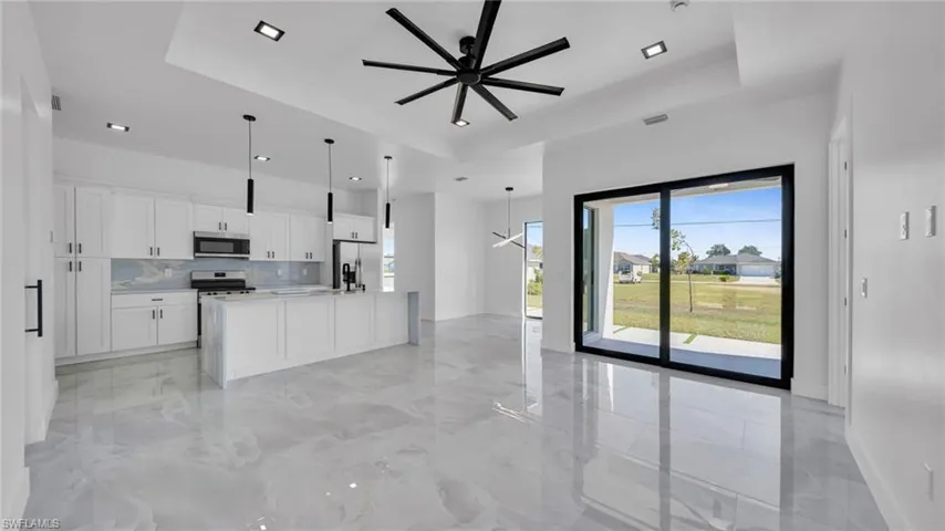 Kitchen with a raised ceiling, white cabinets, decorative backsplash, open floor plan, and a center island with sink