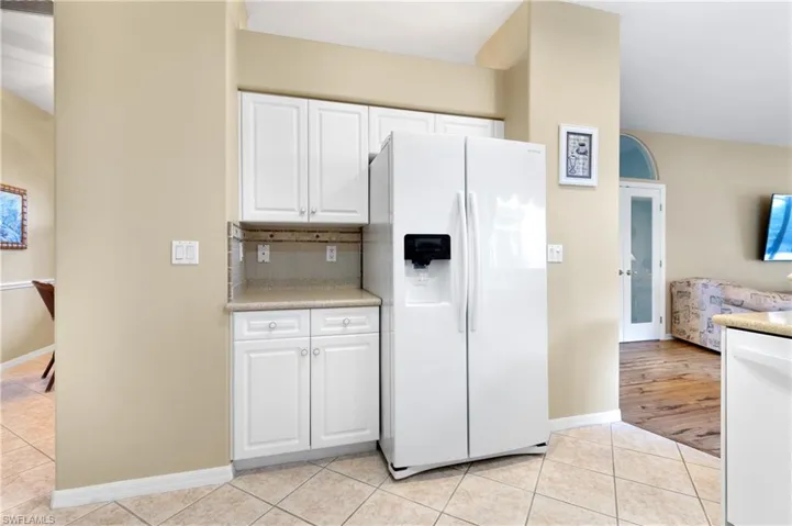 Kitchen featuring backsplash, white refrigerator with ice dispenser, light tile patterned floors, and white cabinets
