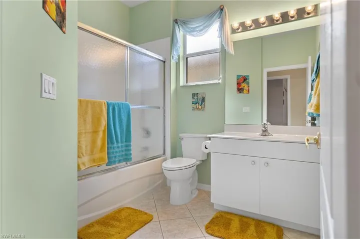 Full bathroom with vanity, tile patterned floors, toilet, and combined bath / shower with glass door