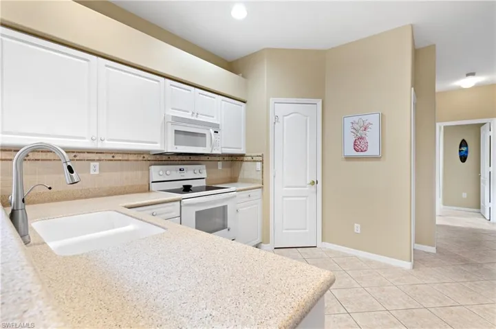 Kitchen featuring light tile patterned flooring, sink, white cabinetry, white appliances, and decorative backsplash