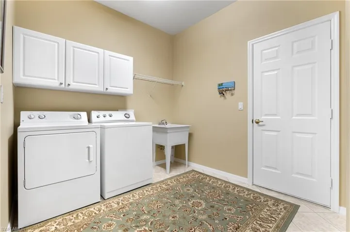 Laundry area with separate washer and dryer, light tile patterned floors, and cabinets