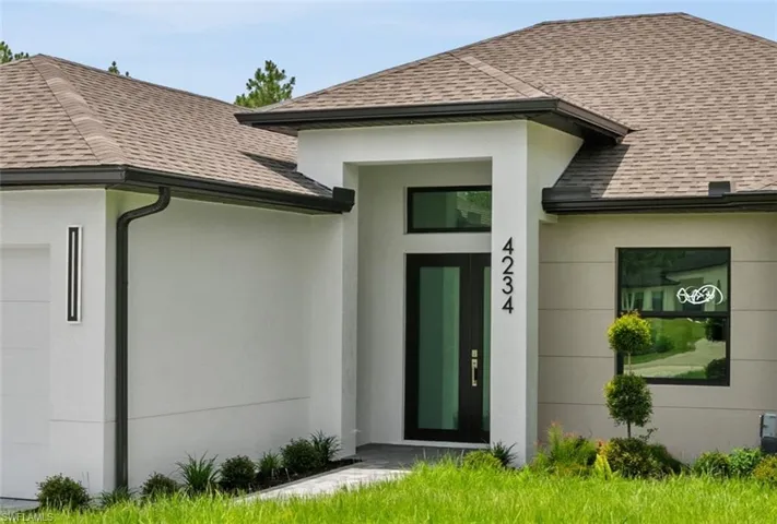 Entrance to property featuring a shingled roof, an attached garage, and stucco siding