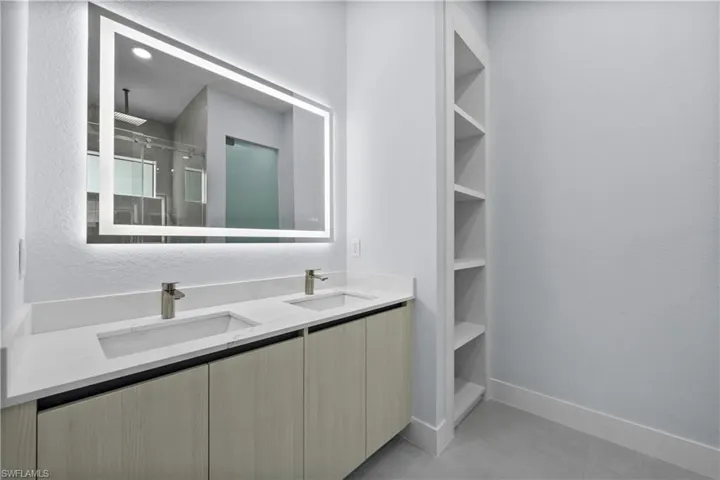 Bathroom with double vanity, a shower stall, a textured wall, and a closet