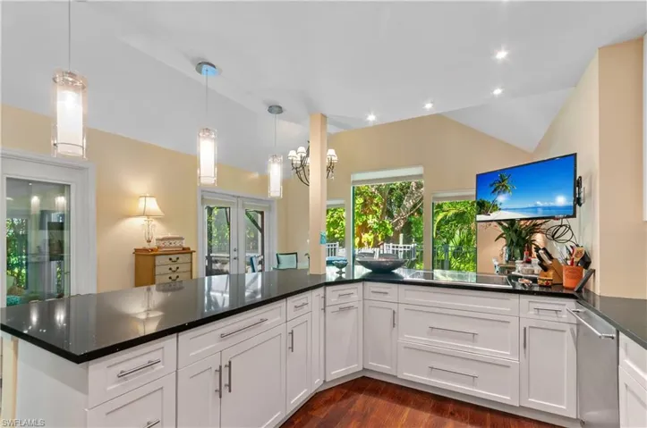 Kitchen with vaulted ceiling, hanging light fixtures, dark stone countertops, dark wood-type flooring, and white cabinetry