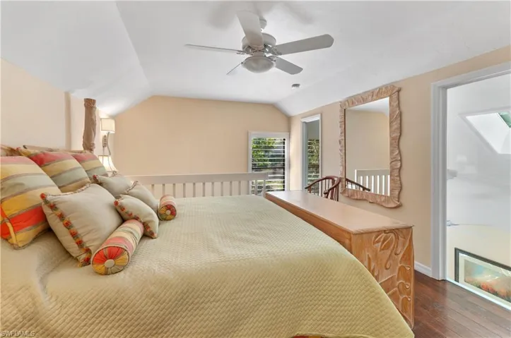 Bedroom with vaulted ceiling, a ceiling fan, and wood finished floors loft above living room stairs