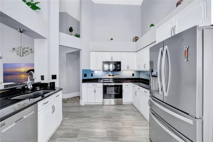 Kitchen featuring white cabinetry, granite counters, stainless appliances, and high ceilings.