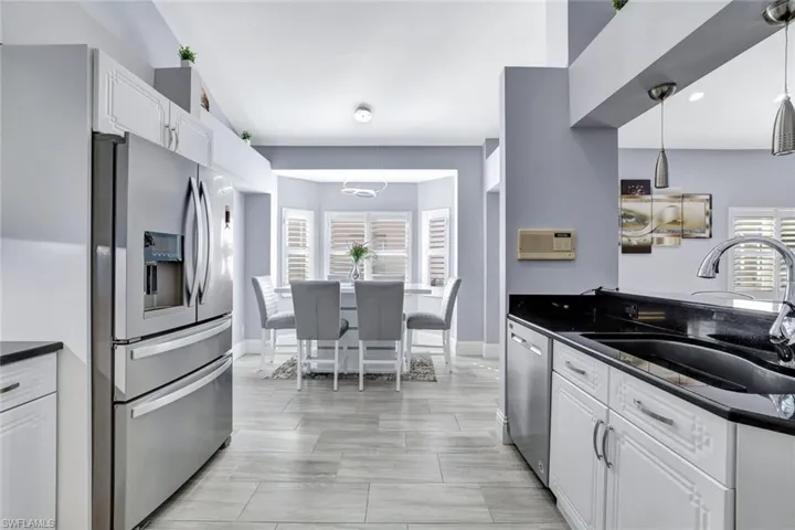 Kitchen view showcasing stainless-steel appliances, granite counters, and a spacious dining nook with plantation-shutter windows.